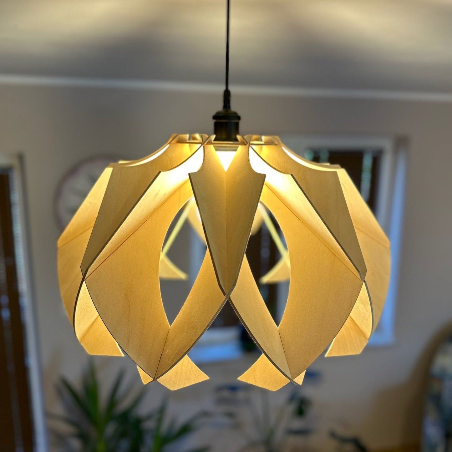 Close-up of a large wooden pendant lamp with a modern, flower-like design. The natural birch wood creates soft, warm light patterns on the ceiling, enhancing the room's ambiance.