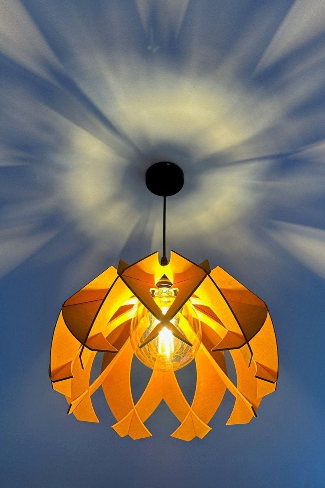Wooden pendant lamp casting beautiful light patterns on the ceiling, featuring a modern flower-shaped design in birch wood.