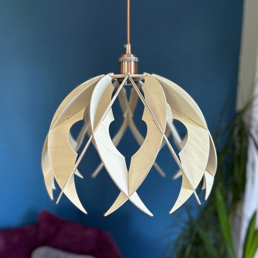 A dome-like wooden pendant light with pointed, curved ribs and circular cutouts, crafted from natural birch wood. Hangs in a cozy living room with teal walls, enhancing the space with its organic, minimalist design and copper cord.