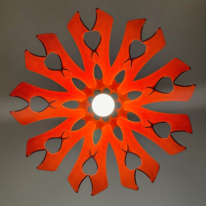 Bottom view of a scarlet-red pendant lampshade with intricate heart-shaped cutouts, creating a floral pattern of light on the ceiling. The bright light source is centered, enhancing the symmetrical design.