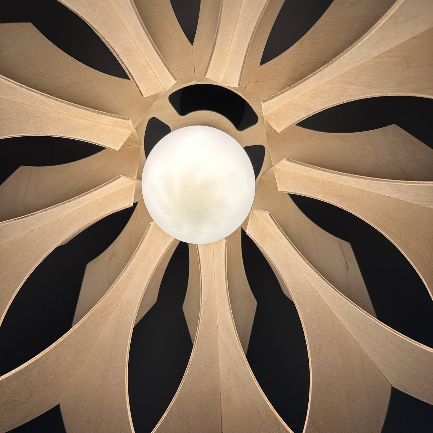 View from below the large wooden pendant lamp, showing the intricate flower-like design and the soft light emitted from a central bulb. The natural wood texture adds warmth to the light.