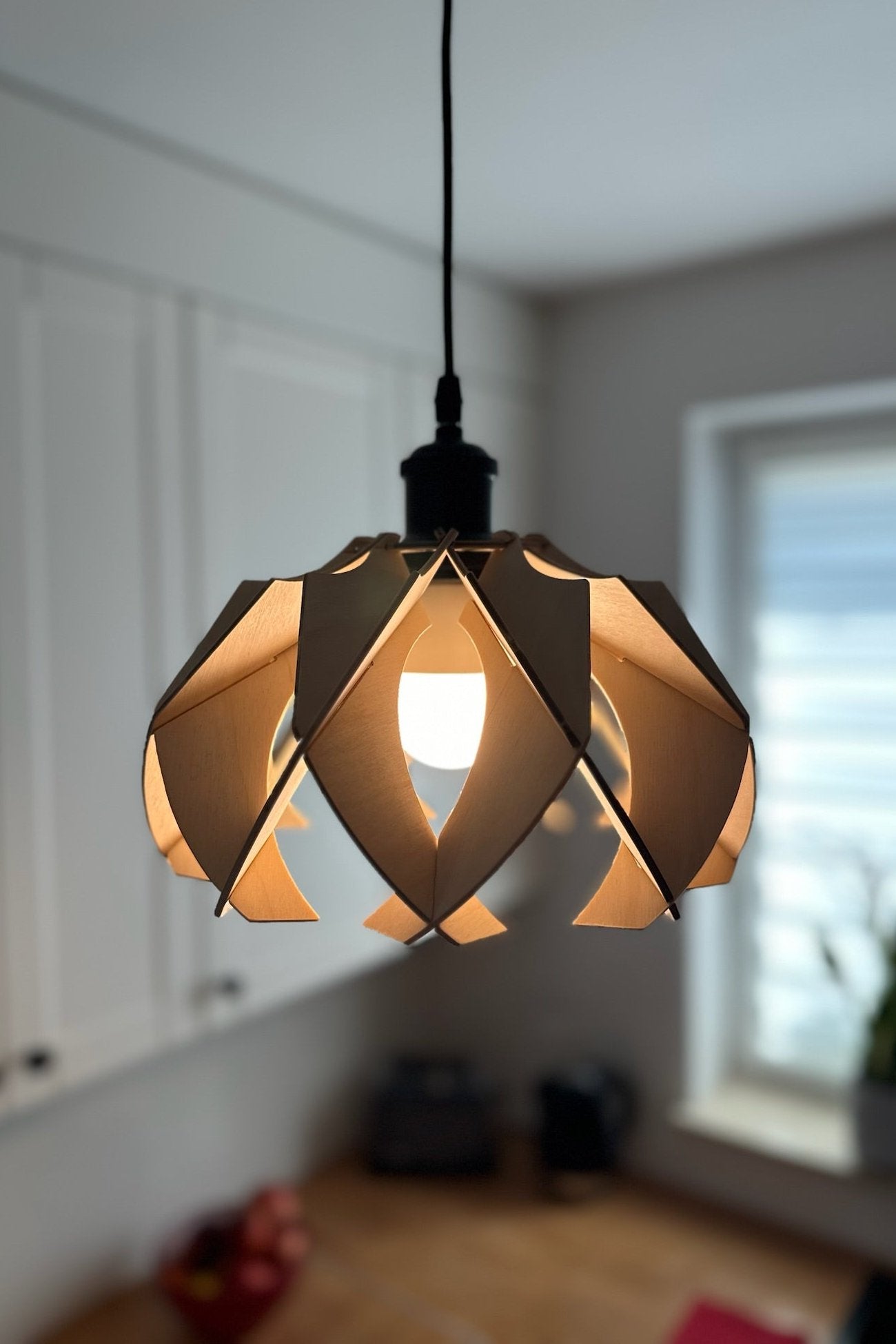 Natural birch wood small pendant lamp hanging in a bright kitchen. The minimalist and modern design highlights the beauty of the wood grain, with the petals curving elegantly to create a soft, ambient light.